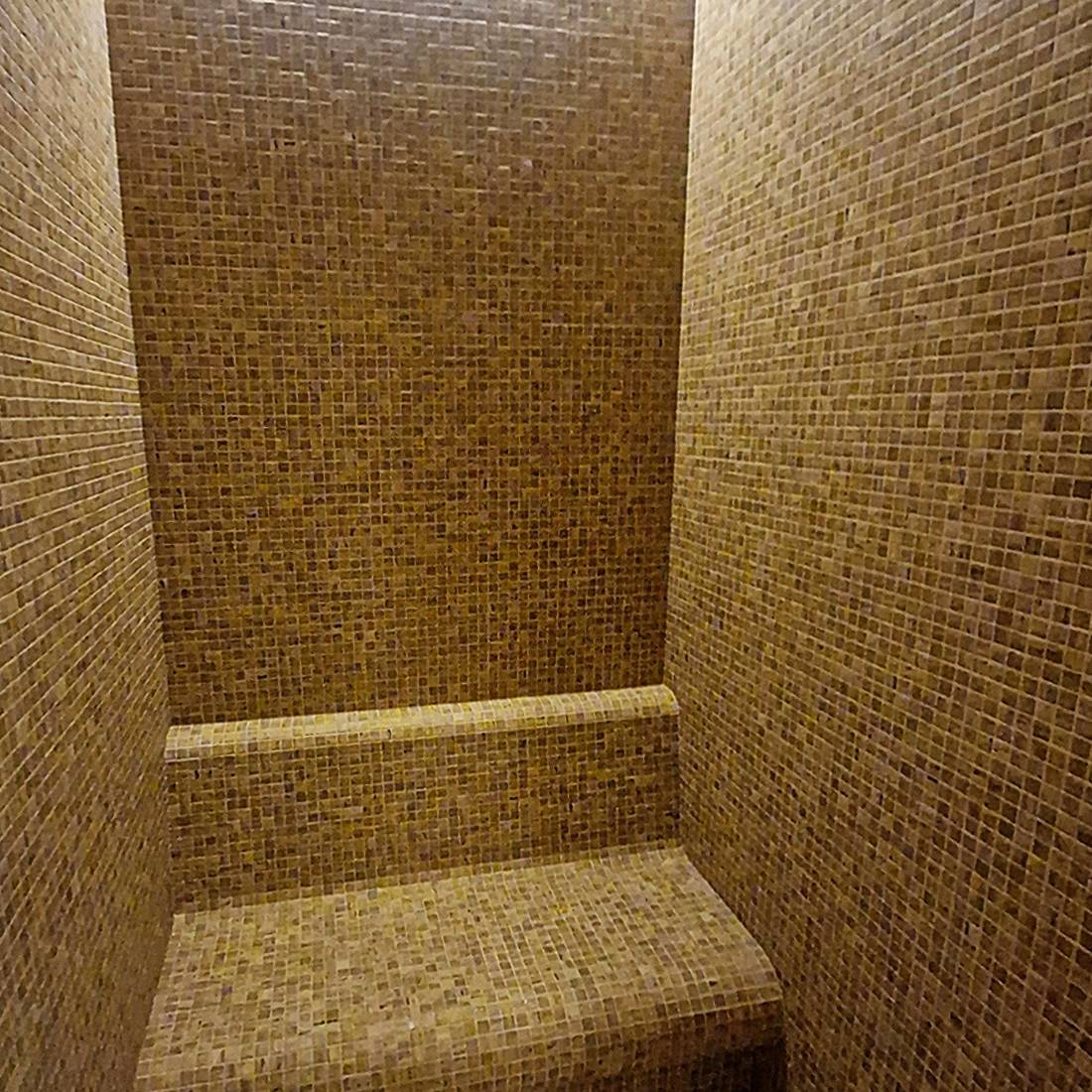 Tiled steam shower with a bench in a bathroom setting