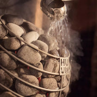 Close up of water being poured on steaming rocks of a HUUM Drop sauna heater