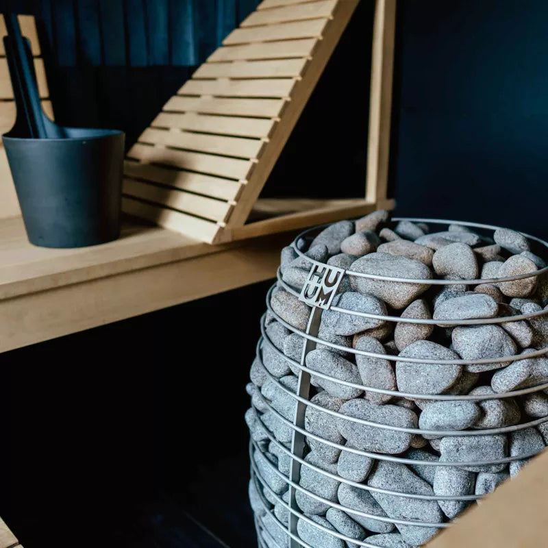 Side view of Huum Hive sauna heater in black sauna with light wooden benches