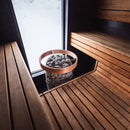 huum hive mini sauna heater with safety rail near  an opaque window in  a sauna with medium brown benches