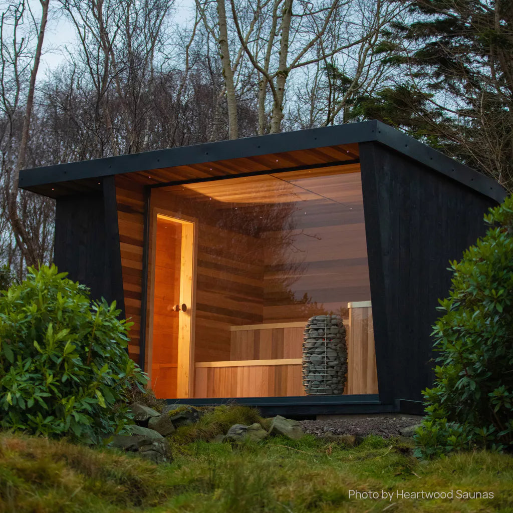 looking into an outdoor sauna located amongst trees with the huum hive mini sauna heater positioned in the glass wall of the sauna visible from the outside