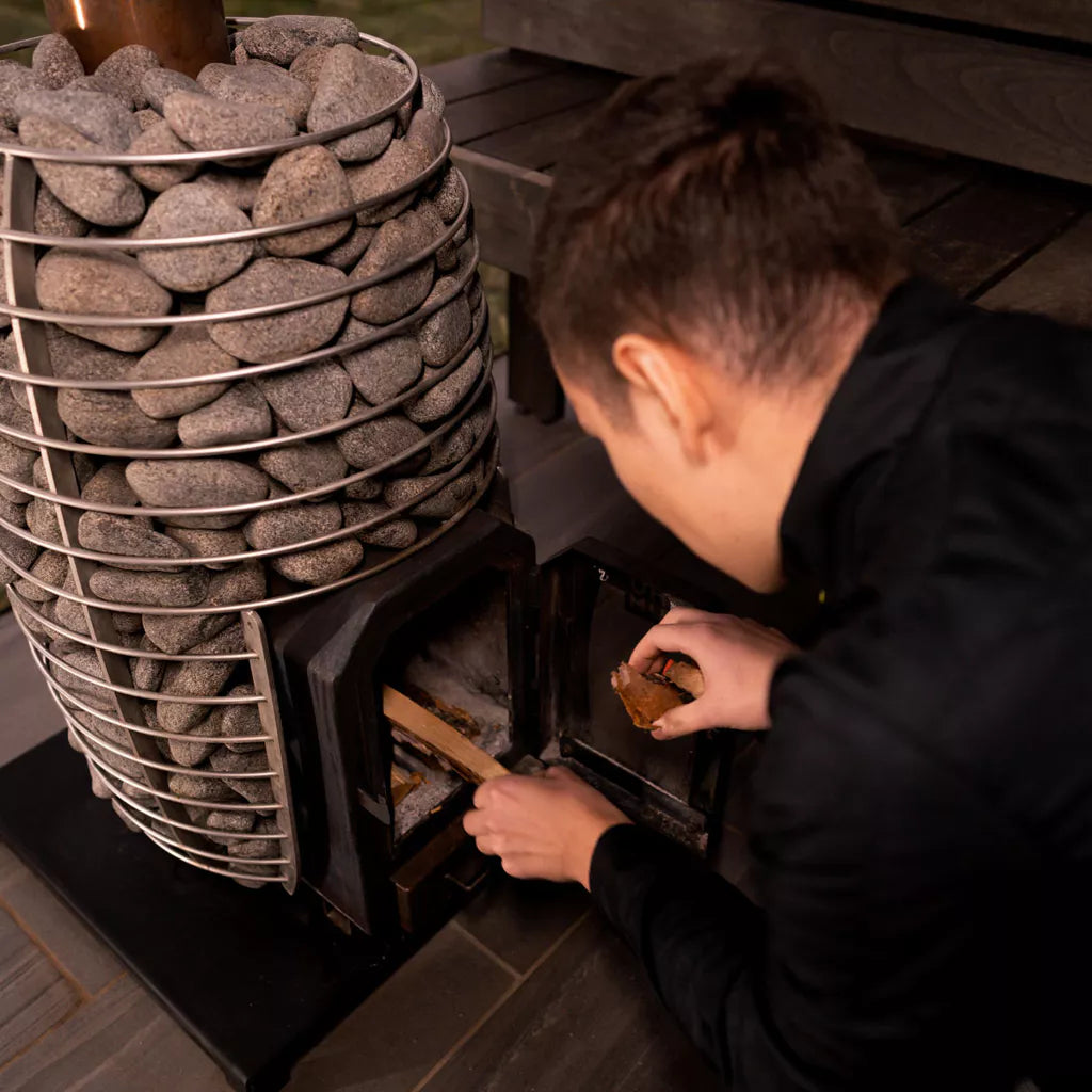 Man loading wood into Huum Hive Wood sauna heater