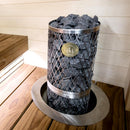 Sauna stove with rocks inside, branded 'iki', in a wooden sauna setting.