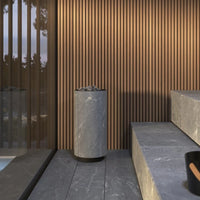 Modern sauna setting with a cylindrical grey sauna heater against a wooden slat wall.
