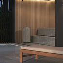 Modern sauna with a wooden bench, stone steps, and a wall with vertical slats with a grey cyclindrical sauna heater in front of it.