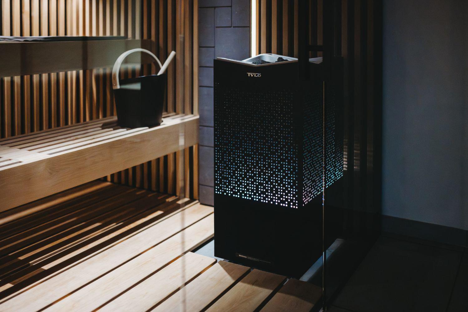 Tylo Crown combi elite sauna heater against wall of heater with built-in lights glowing through aluminium grill