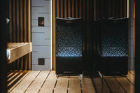 Tylo Crown elite electric sauna heater positioned on floor of dimly lit sauna and reflected in the glass