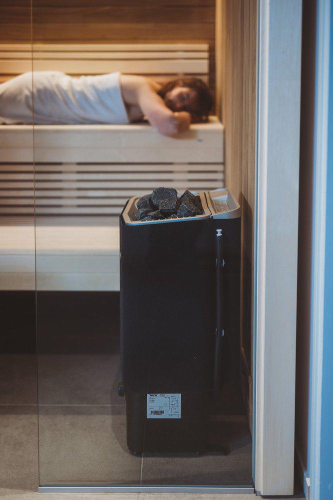 Side view of Tylo sense combi pure sauna heater with woman relaxing on sauna bench in background