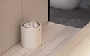 A minimalist cylindrical sauna heater  filled with white decorative stones, set on a light wood plank floor in a modern bathroom interior.