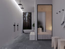 A modern minimalist bathroom interior with dark gray stone tile flooring, white walls, matte black fixtures, and a large black-framed mirror reflecting a spa-like treatment room. A freestanding oval bathtub is visible in the background near a window showing a forest view and a white cylindrical sauna heater in adjacent room