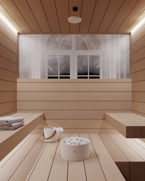 A minimalist wooden sauna interior with tiered seating, a white stone sauna heater filled with white stones, folded towels on the side, and a large window with sheer curtains in the background.