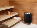 Sauna interior with wooden benches, a black sauna heater, and a copper bucket.