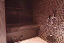 Corner of a steam room with tiled walls and a handheld shower head with Bahia Home below the shower head fixed to the wall